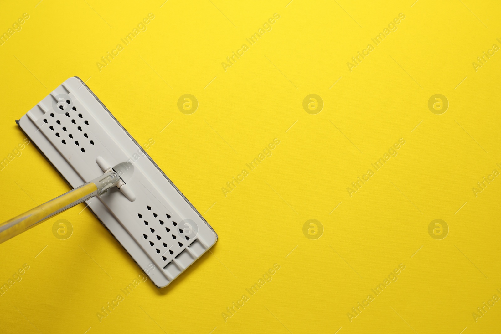 Photo of Mop with metal handle on yellow background, top view. Space for text