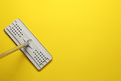 Mop with metal handle on yellow background, top view. Space for text