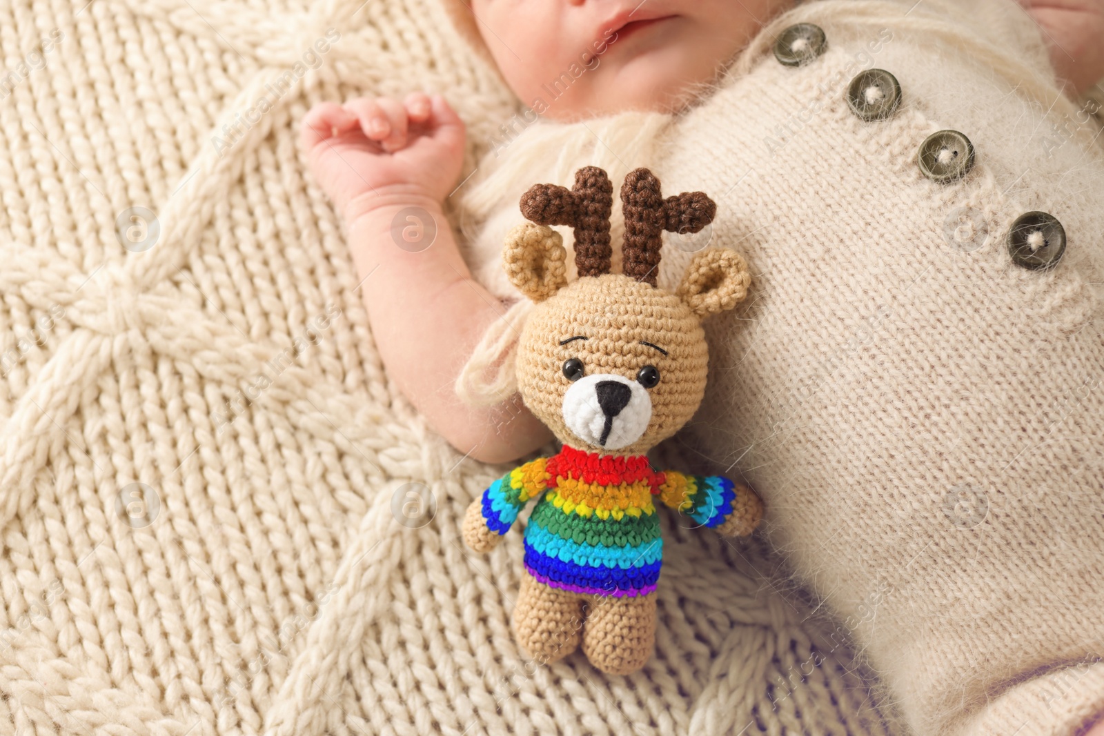 Image of National rainbow baby day. Little child with knitted toy sleeping on blanket, closeup