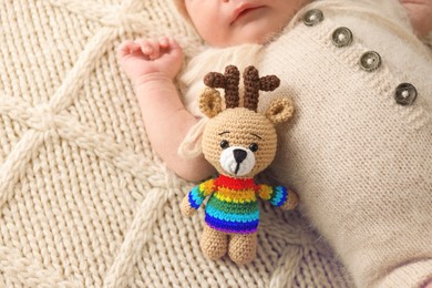 Image of National rainbow baby day. Little child with knitted toy sleeping on blanket, closeup