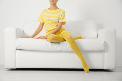 Photo of Woman wearing yellow tights sitting on sofa indoors, closeup