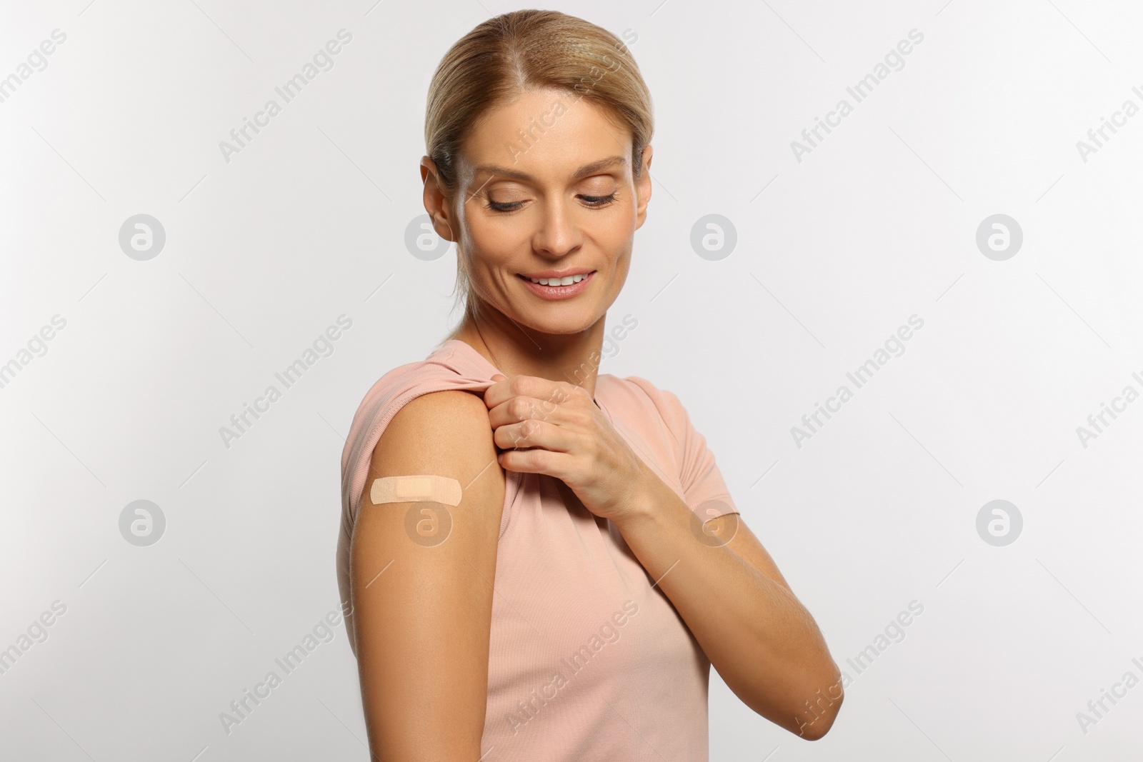 Photo of Smiling woman with adhesive bandage on arm after vaccination on light background