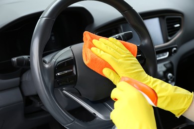 Photo of Woman cleaning steering wheel with rag in car, closeup