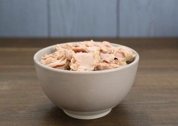 Photo of Bowl with canned tuna on wooden table, closeup