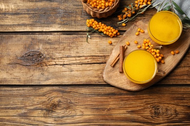 Sea buckthorn tea and fresh berries on wooden table, flat lay. Space for text