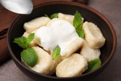 Photo of Bowl of tasty lazy dumplings with sour cream and mint leaves on brown table, closeup