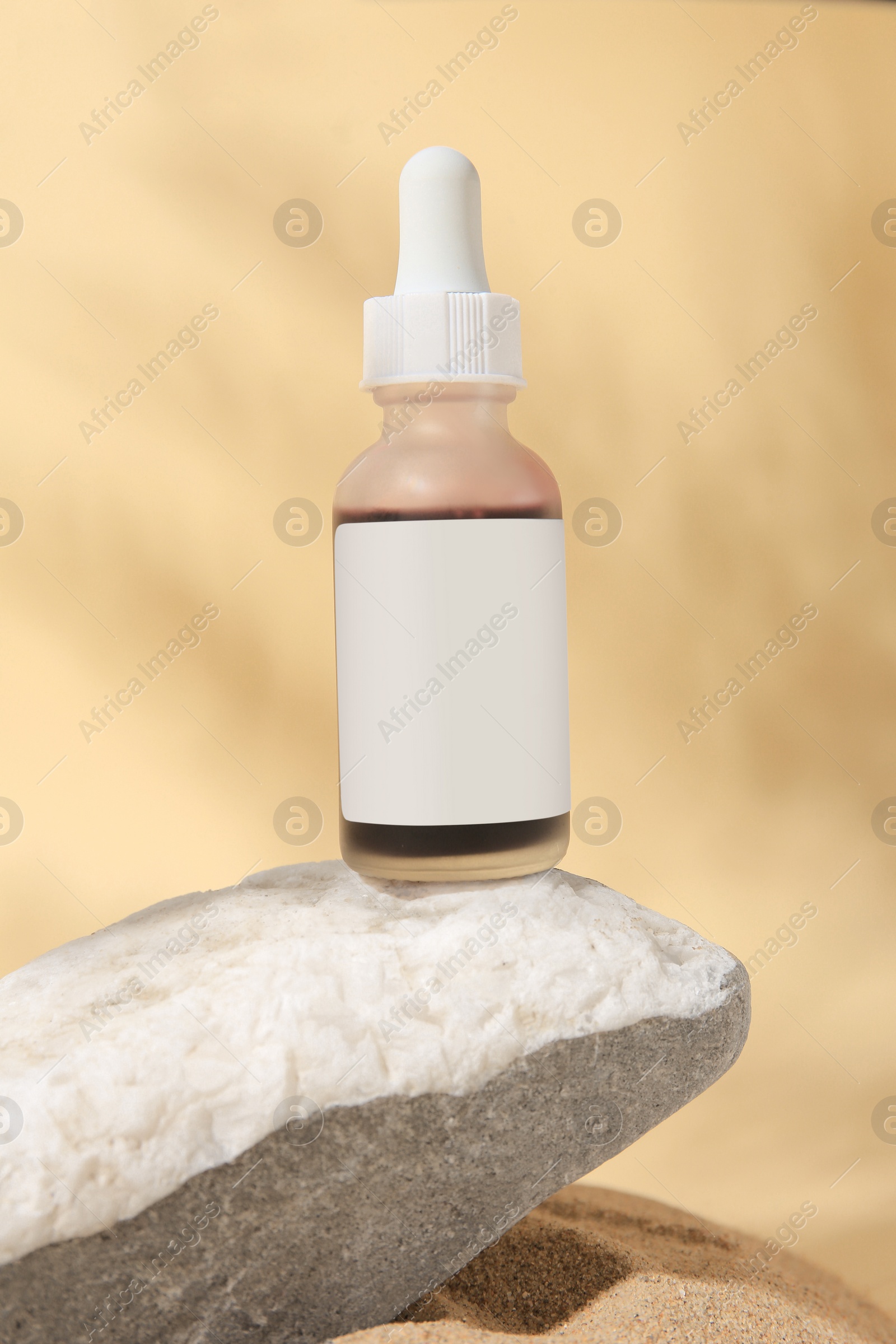 Photo of Bottle of serum and stone on sand against beige background