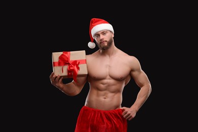 Photo of Attractive young man with muscular body holding Christmas gift box on black background