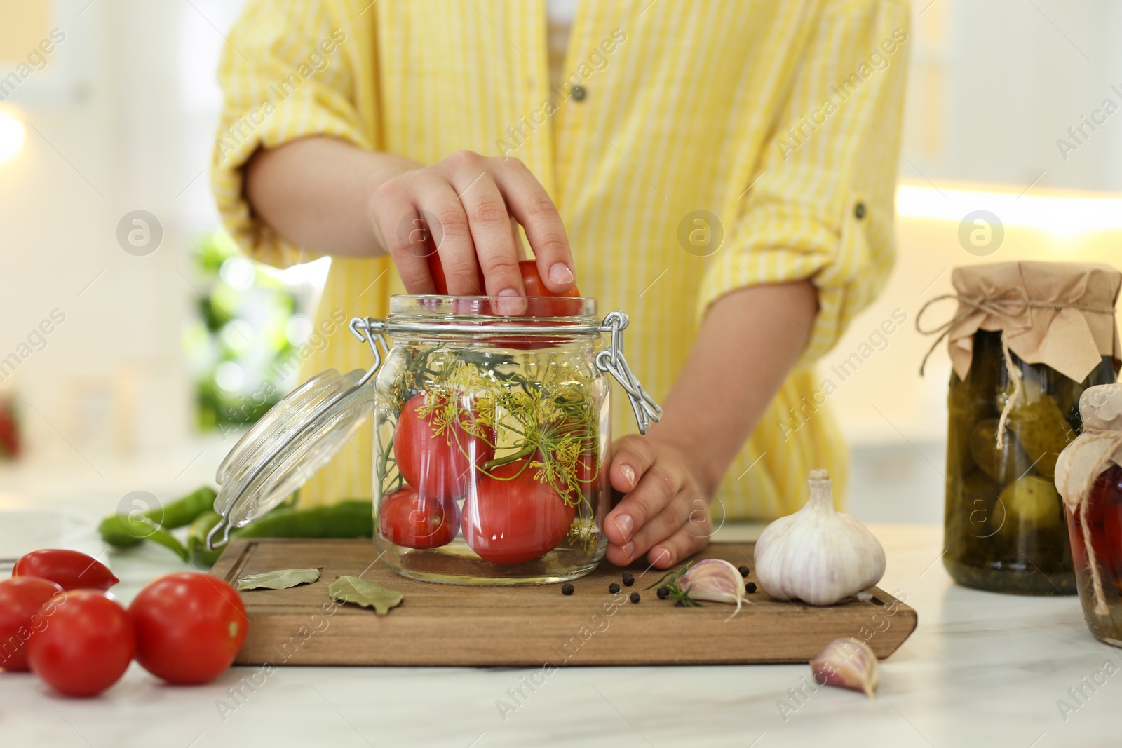 Photo of Woman putting tomatoes into pickling jar at kitchen table, closeup