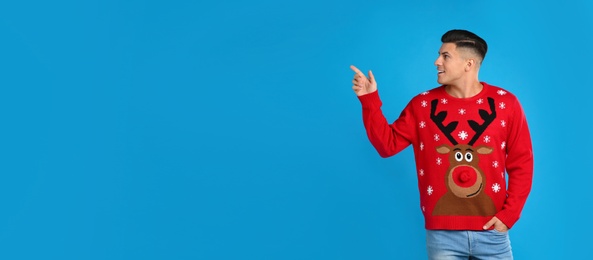 Photo of Handsome man in Christmas sweater pointing on blue background, space for text