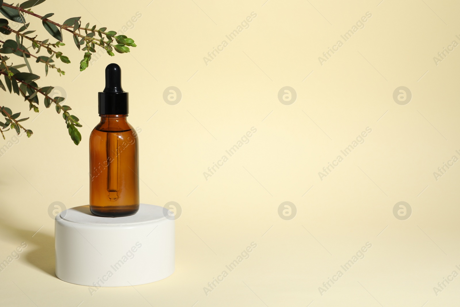 Photo of Bottle with cosmetic oil on podium and green branch on beige background, space for text