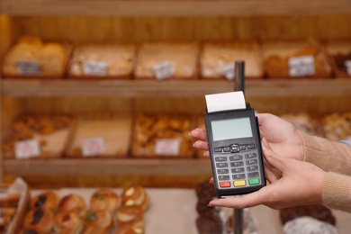 Woman holding payment terminal in bakery, closeup. Space for text