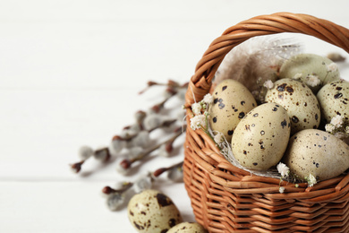 Photo of Closeup view of quail eggs and flowers in wicker basket on white table, space for text. Easter celebration