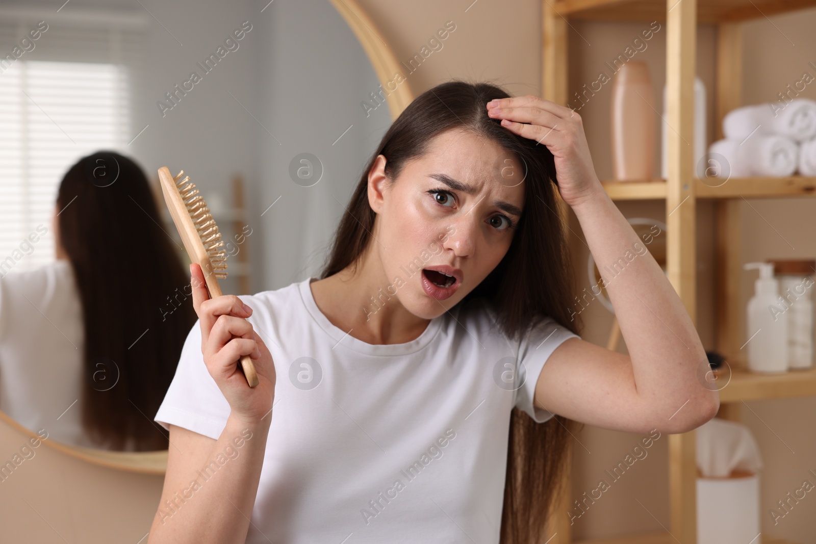 Photo of Emotional woman with brush examining her hair in bathroom. Dandruff problem