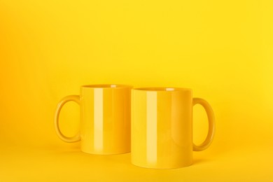 Photo of Two blank ceramic mugs on yellow background