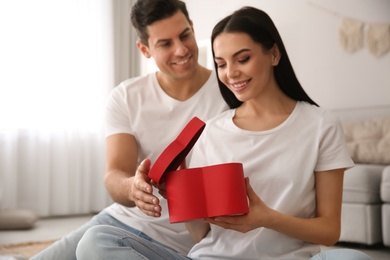 Photo of Lovely couple with gift at home, focus on box. Valentine's day celebration