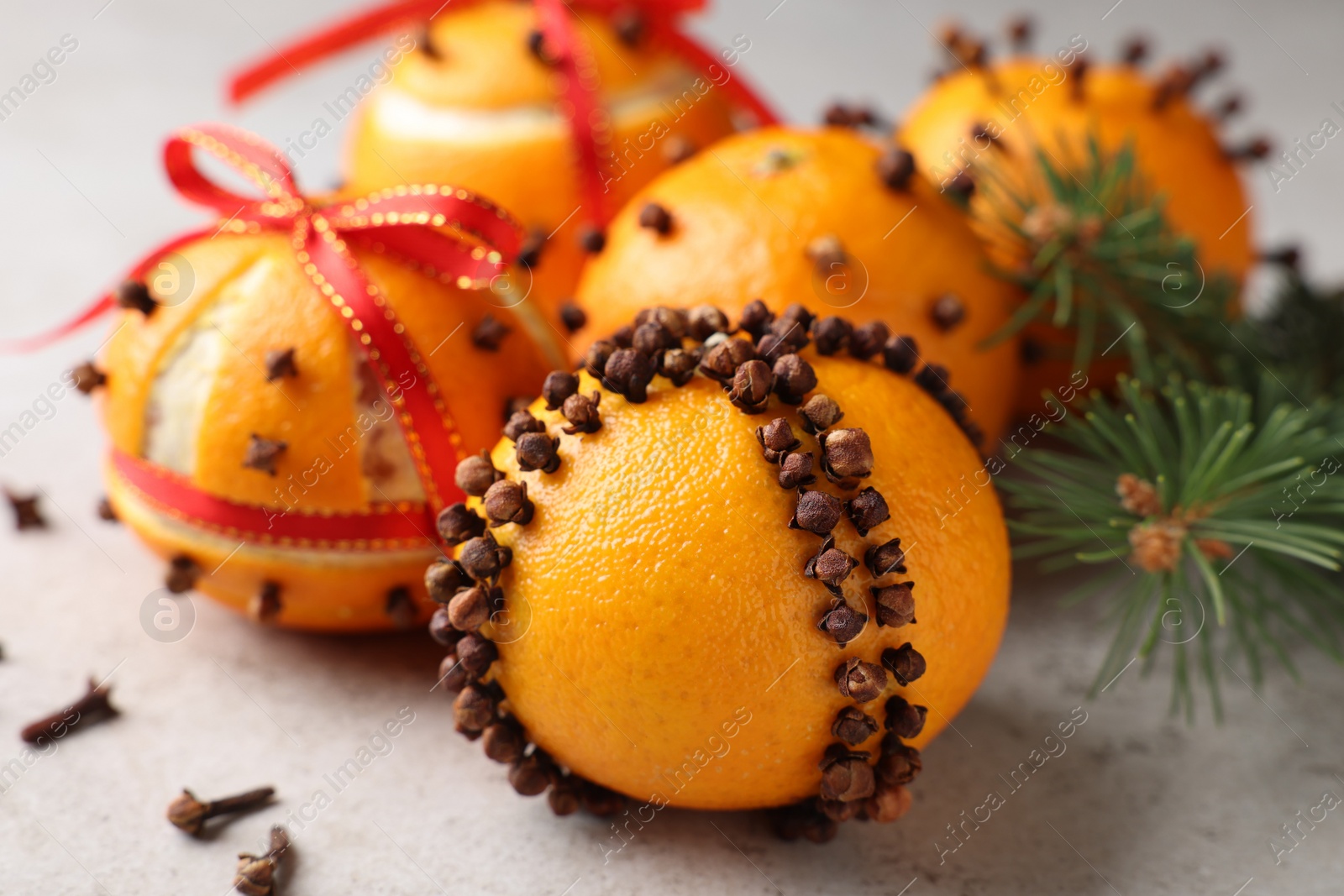 Photo of Pomander balls made of tangerines with cloves and fir branch on grey table, closeup
