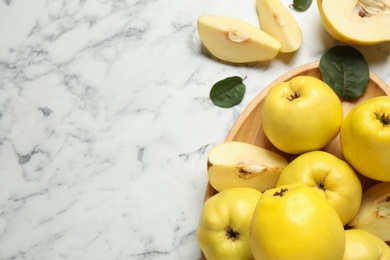 Photo of Fresh ripe organic quinces with leaves on white marble table, flat lay. Space for text