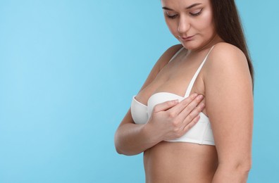 Mammology. Woman in bra doing breast self-examination on light blue background