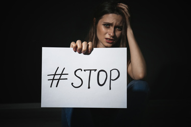 Photo of Crying young woman with hashtag STOP on black background. Domestic violence concept