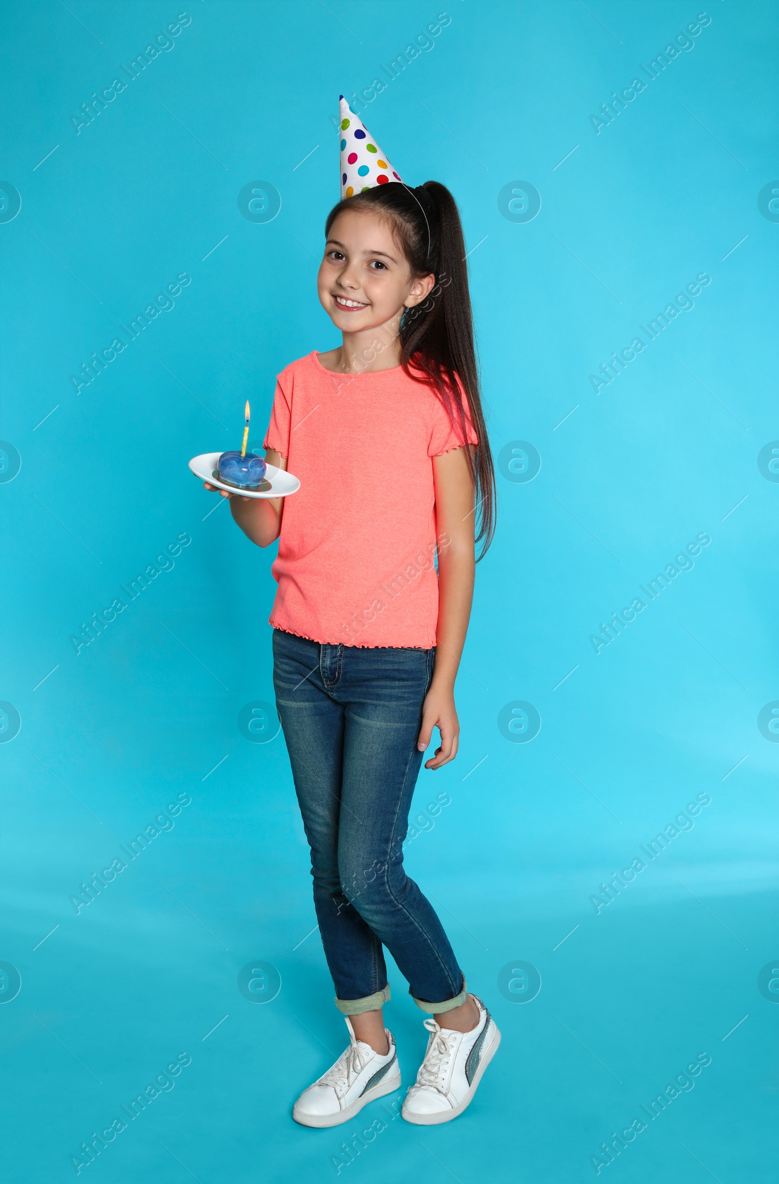 Photo of Happy girl holding birthday sweetness with candle on blue background