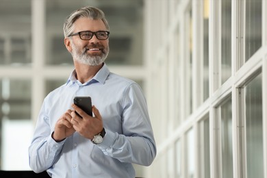 Photo of Smiling man with smartphone in office, low angle view. Lawyer, businessman, accountant or manager