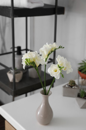 Beautiful freesia flowers in vase on white table indoors