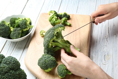 Photo of Woman cutting fresh green broccoli with knife on white wooden table, closeup view