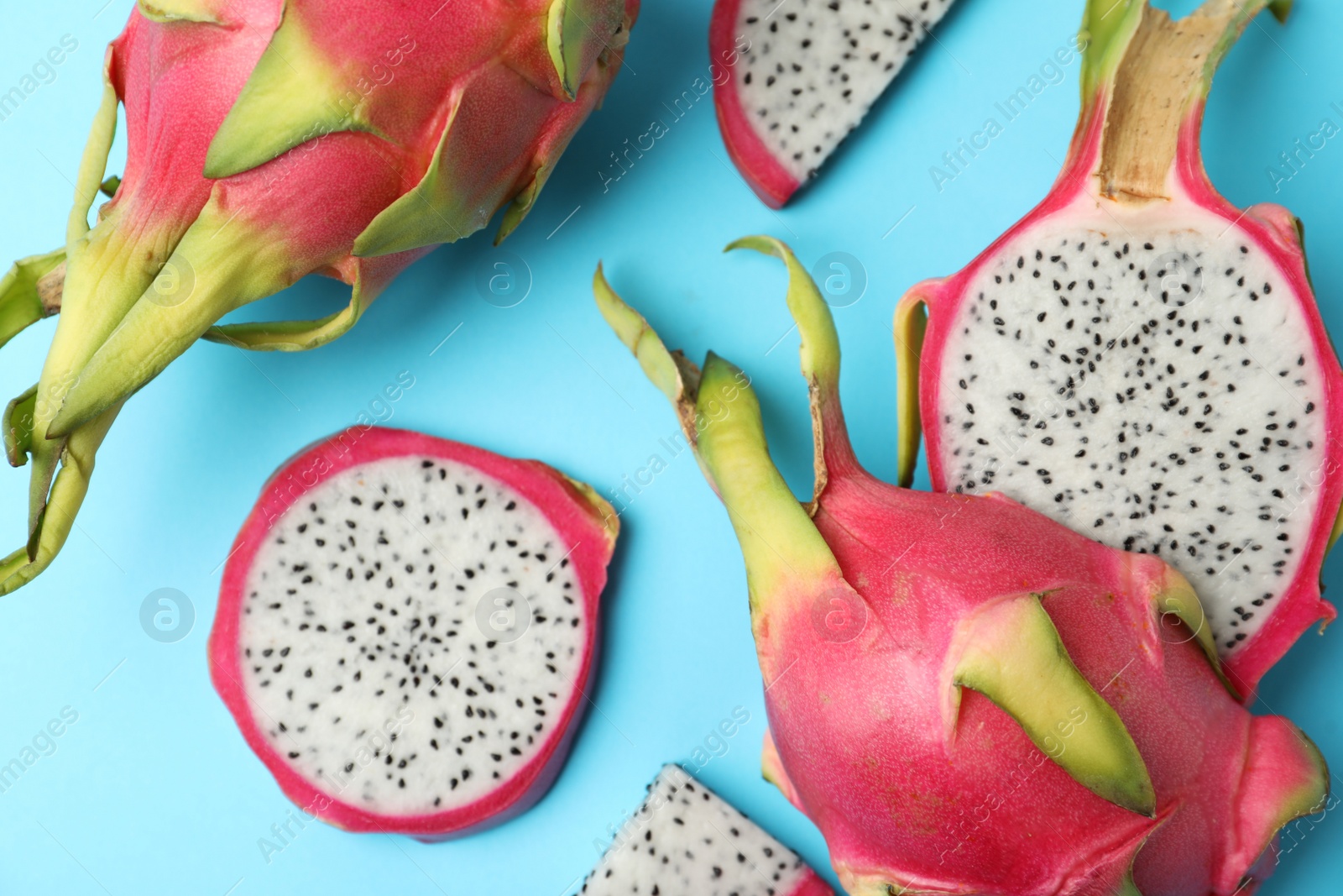 Photo of Delicious cut and whole dragon fruits (pitahaya) on light blue background, flat lay