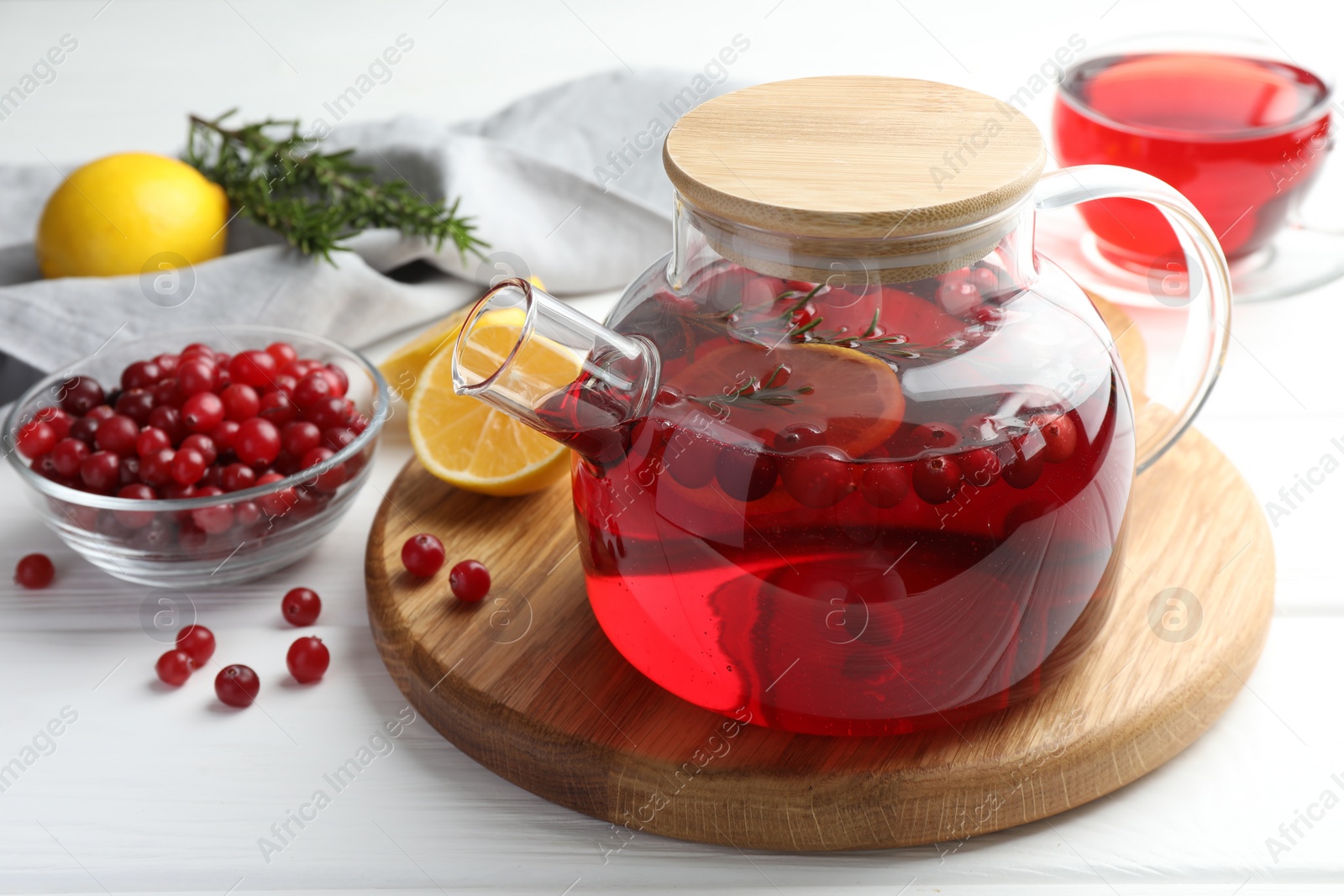 Photo of Tasty hot cranberry tea in teapot, lemon and fresh berries on white wooden table