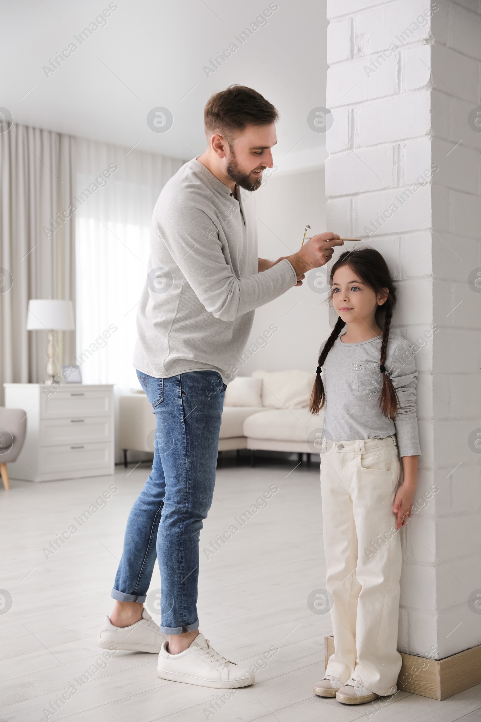 Photo of Father measuring daughter's height near white brick pillar at home