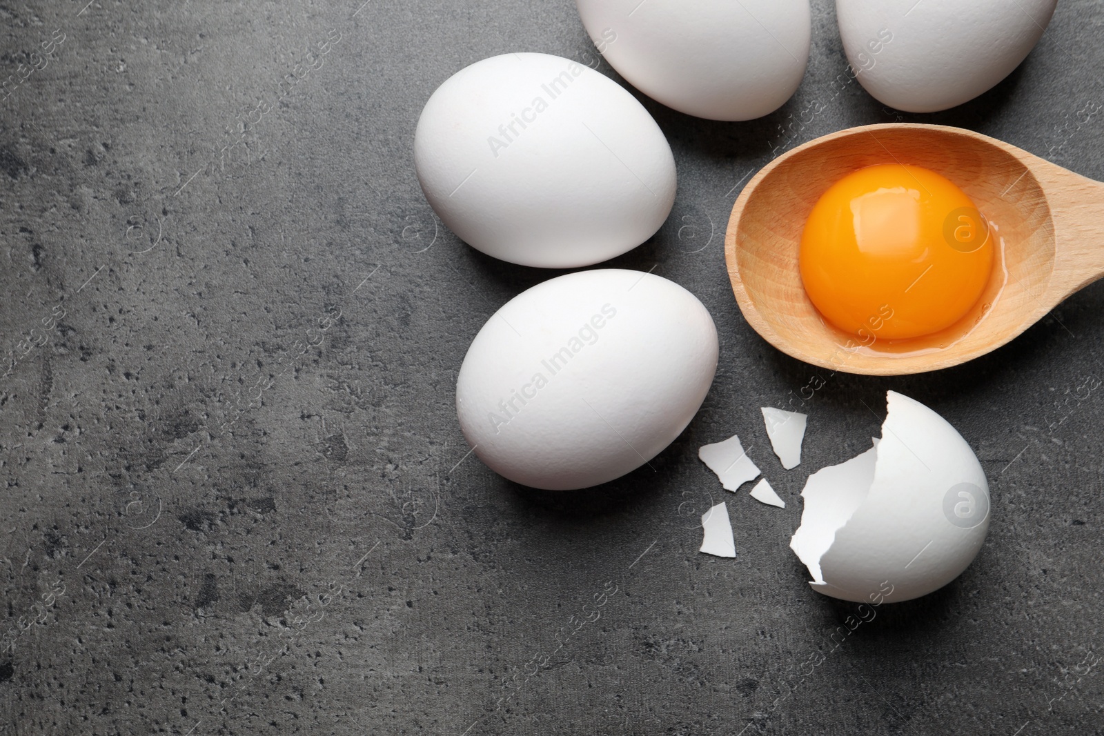 Photo of Raw chicken eggs and spoon with yolk on grey table, flat lay. Space for text