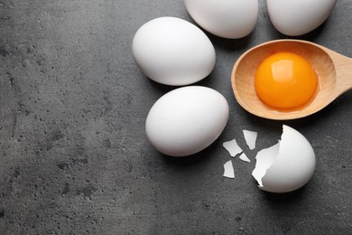 Photo of Raw chicken eggs and spoon with yolk on grey table, flat lay. Space for text