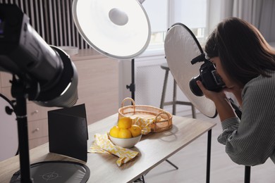 Photo of Young woman with professional camera taking photo of lemons in studio