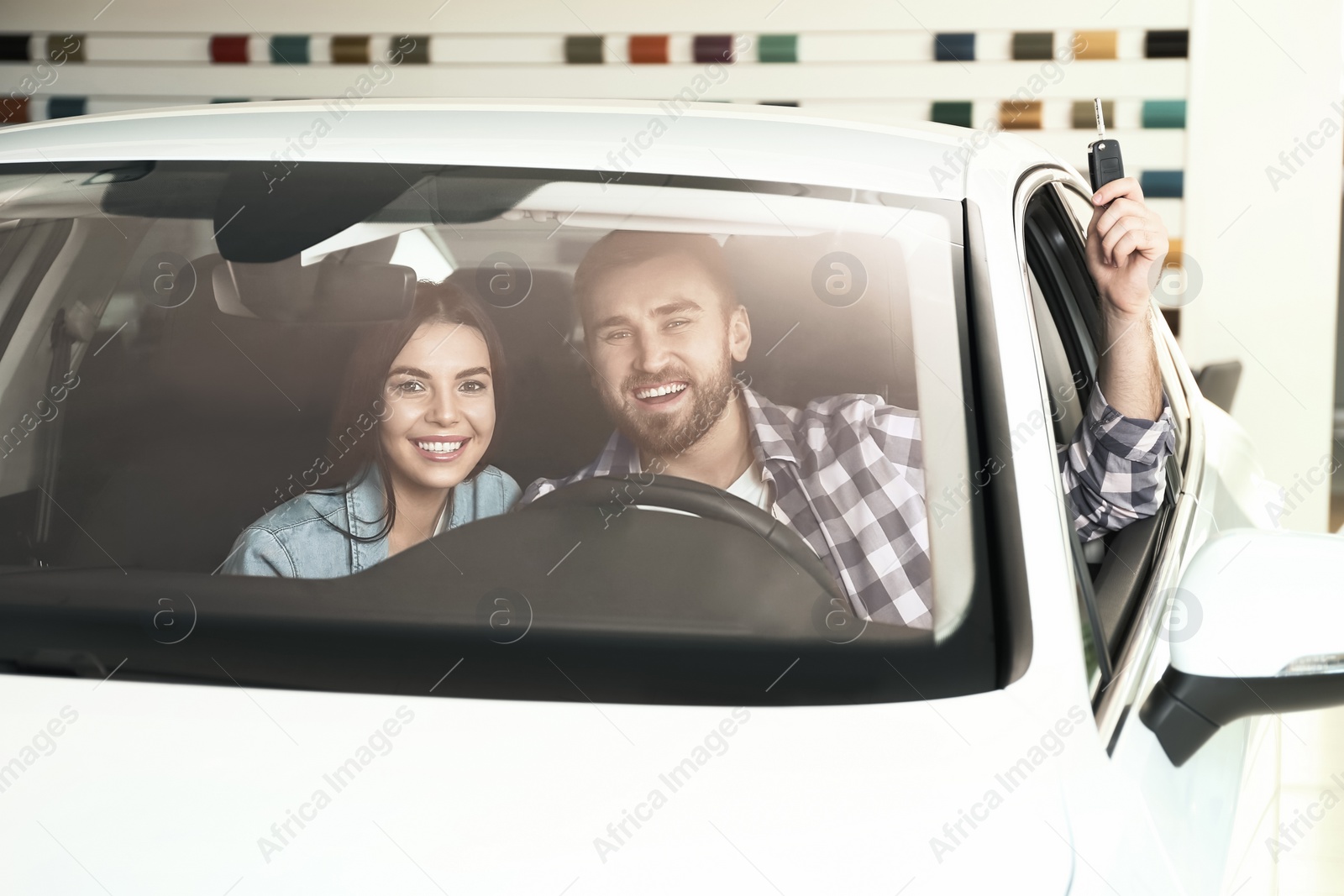 Photo of Happy couple with car key sitting in modern auto at dealership