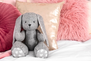 Photo of Cute toy rabbit on bed in child's room interior. Space for text