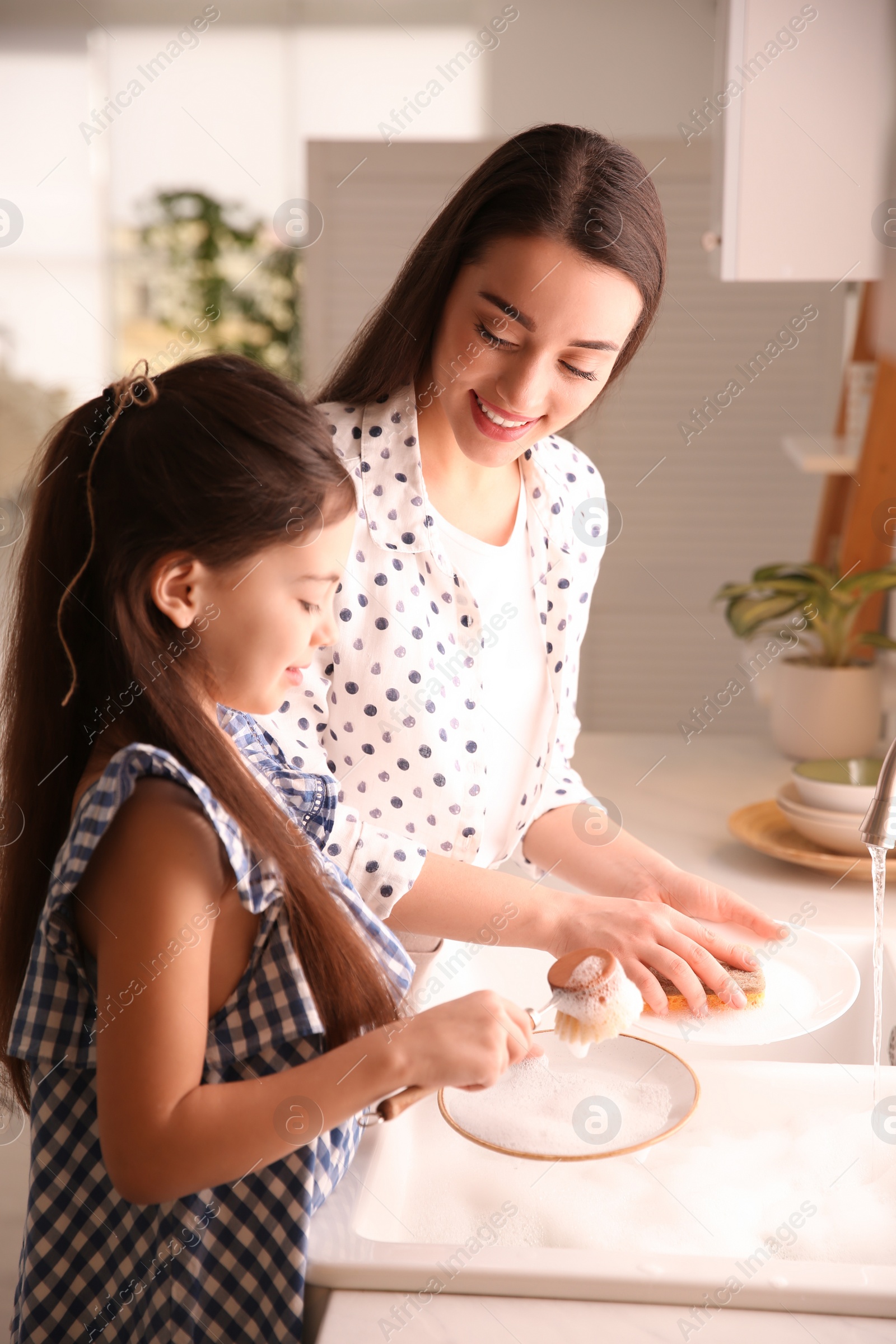 Photo of Mother and daughter washing dishes together in kitchen