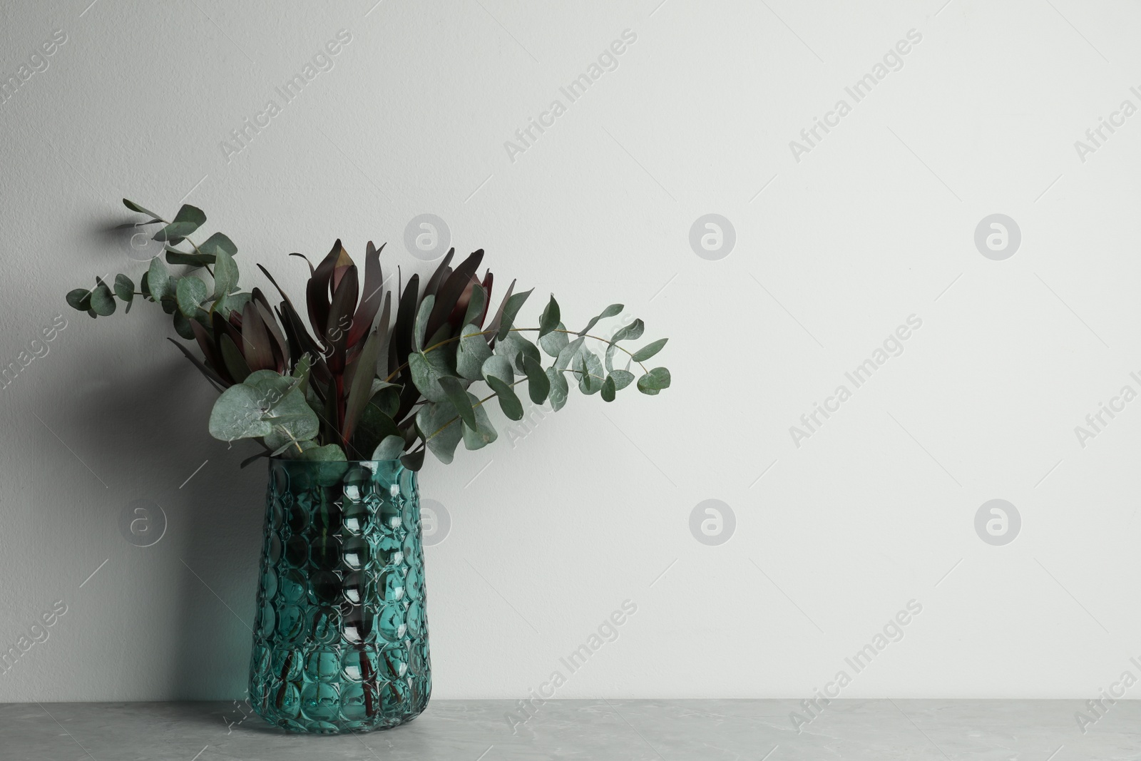 Photo of Bouquet of beautiful protea flowers and eucalyptus branches in glass vase on grey table against white background. Space for text