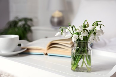 Photo of Beautiful snowdrops, book and cup of coffee on tray in bedroom. Space for text