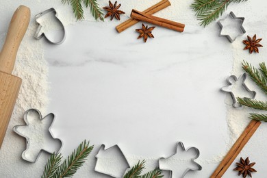 Frame of cookie cutters, cinnamon sticks, flour and anise stars on white marble table, flat lay. Space for text