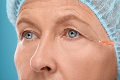 Photo of Senior woman getting facial injection on light blue background, closeup. Cosmetic surgery