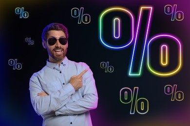 Image of Discount offer. Happy man pointing at percent signs on dark background