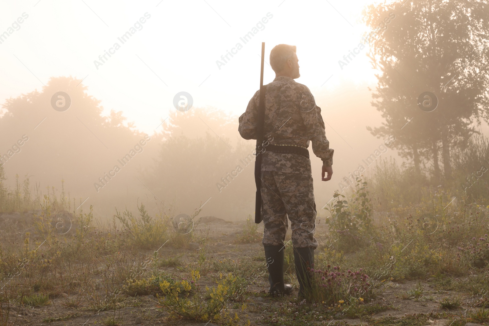 Photo of Man with hunting rifle wearing camouflage outdoors, back view. Space for text