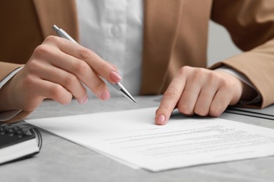 Woman signing document at light grey marble table, closeup