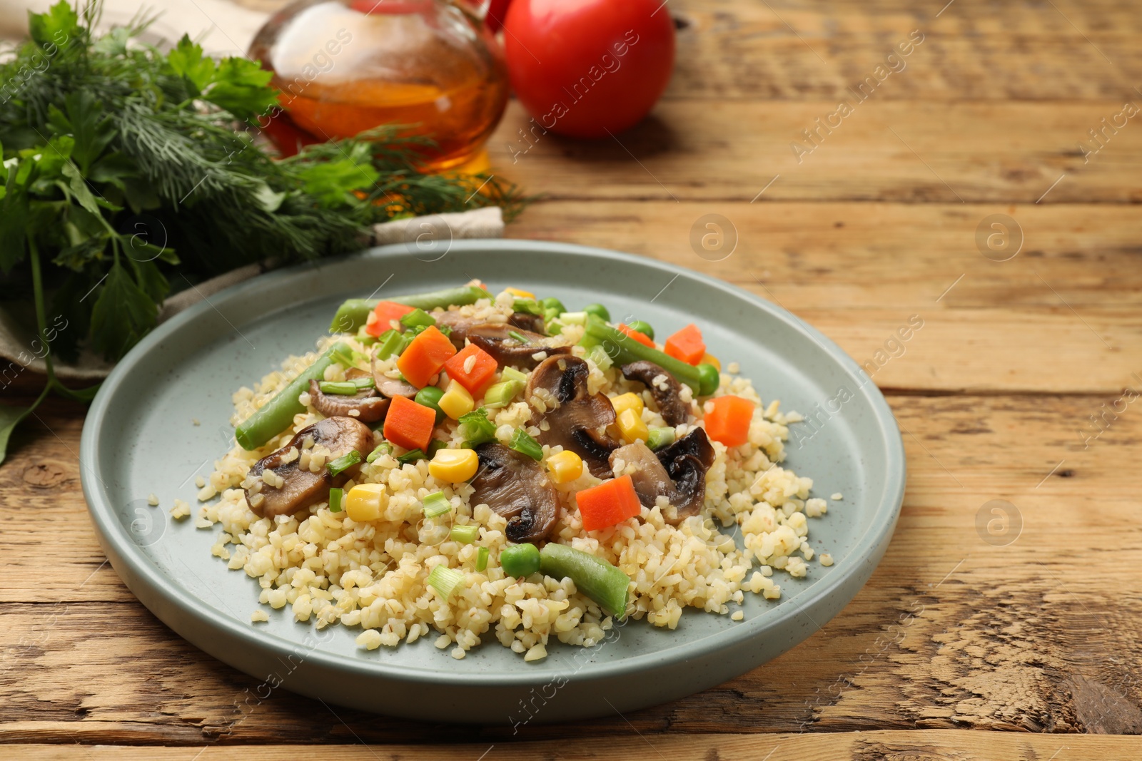 Photo of Delicious bulgur with vegetables and mushrooms on wooden table, closeup