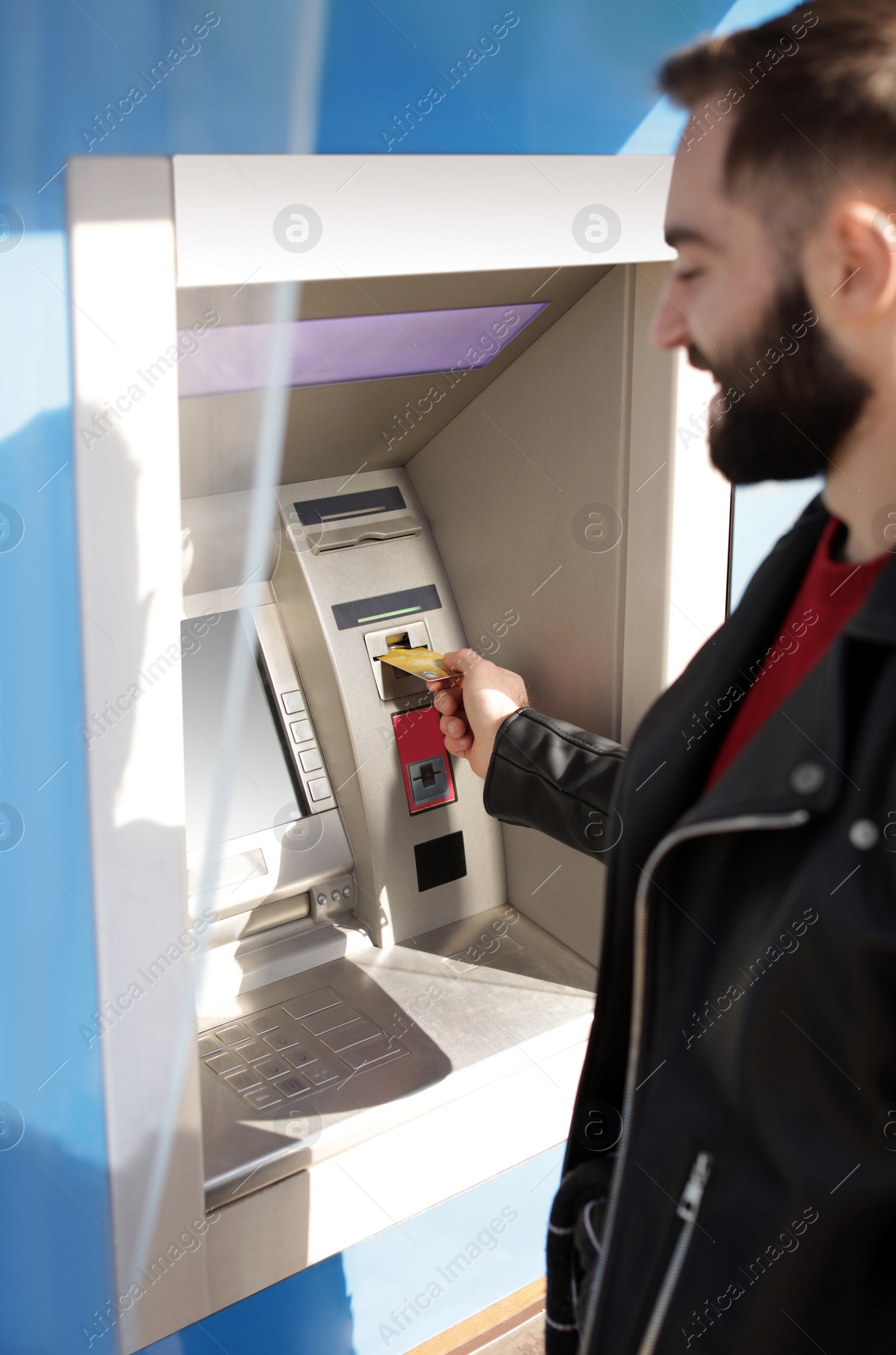 Photo of Young man inserting credit card into cash machine outdoors