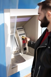 Photo of Young man inserting credit card into cash machine outdoors