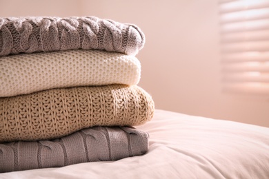 Photo of Stack of folded warm sweaters on bed indoors, closeup. Space for text