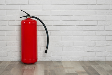 Photo of Fire extinguisher near white brick wall indoors, space for text