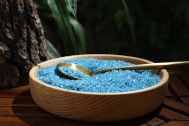 Photo of Bowl of blue sea salt with spoon on wooden table, closeup